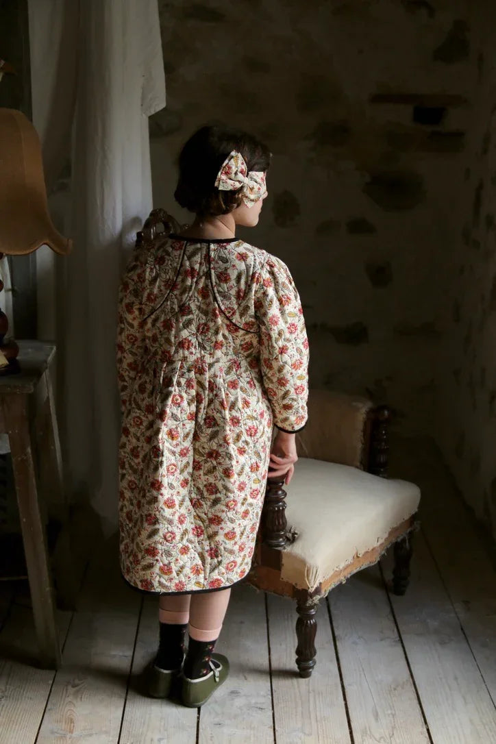 Child wearing floral print nightgown and matching hair bow in vintage room setting