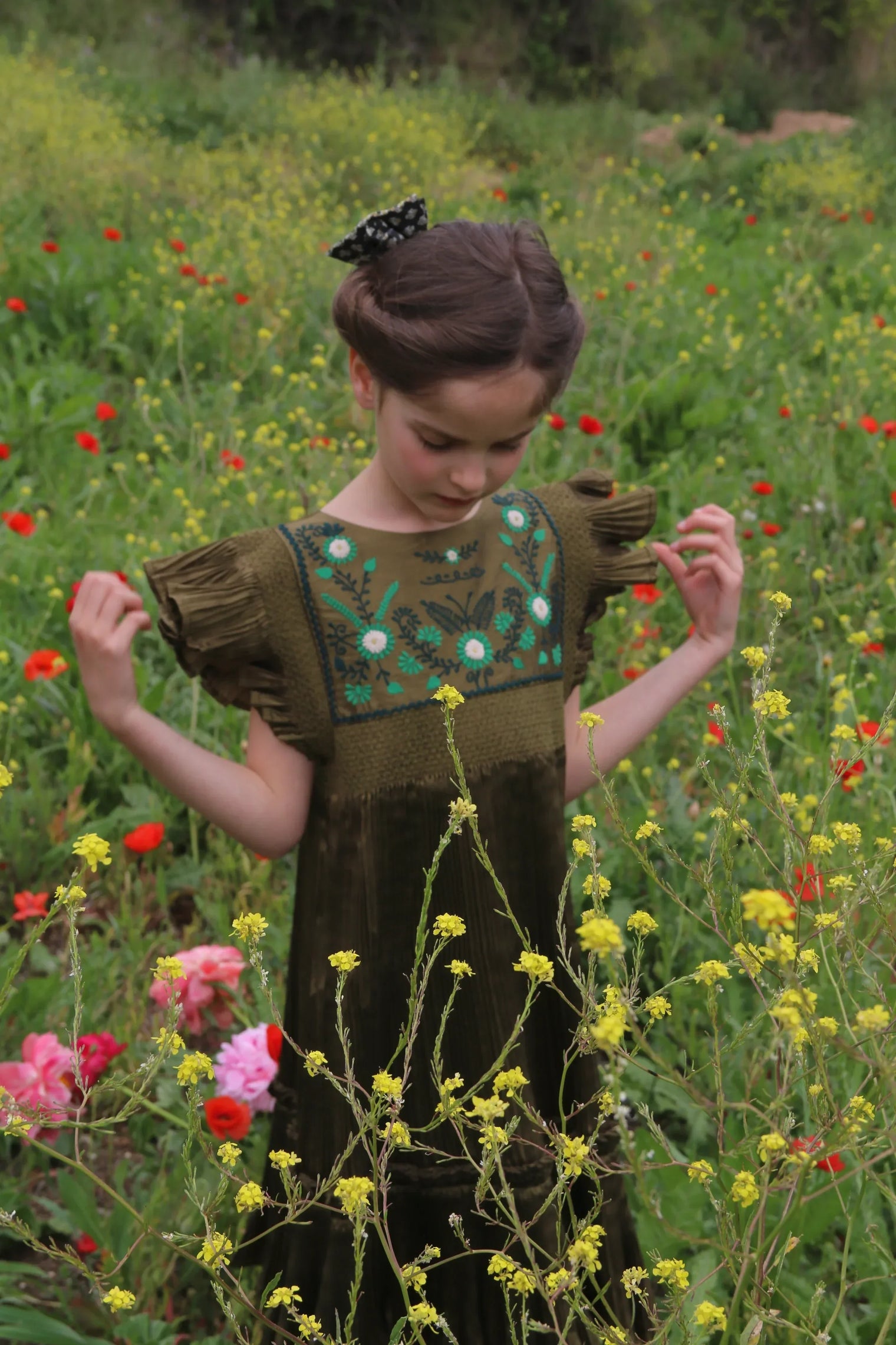 Girl in olive green embroidered dress standing in a field of wildflowers