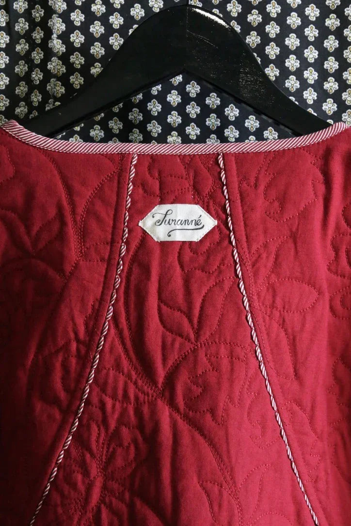 Red quilted children’s dress with floral stitching, label detail, and striped trim on hanger