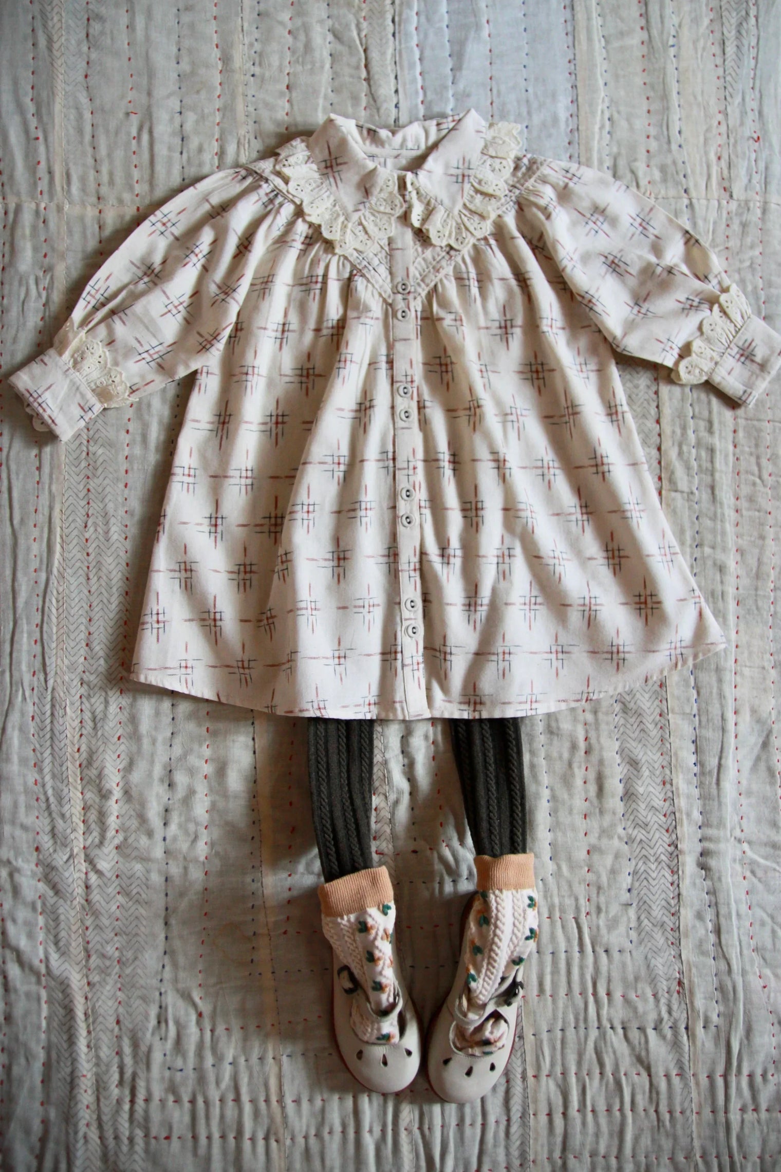 Vintage style girls dress with lace collar, patterned tights, and decorative shoes laid on quilt.
