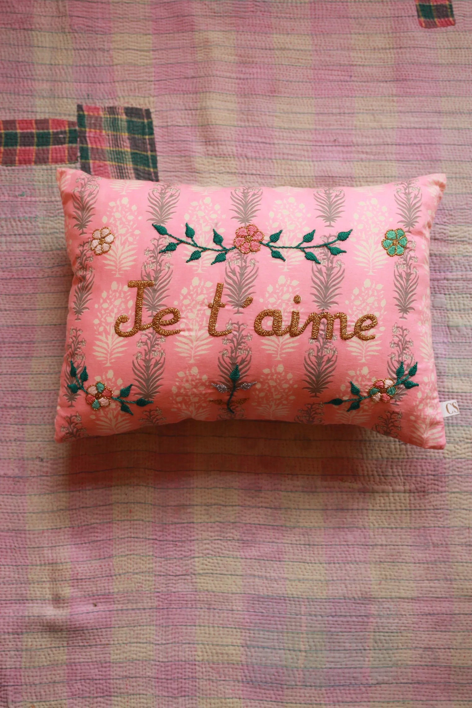 Pink embroidered cushion with 'Je t'aime' text and floral design on a pastel quilt