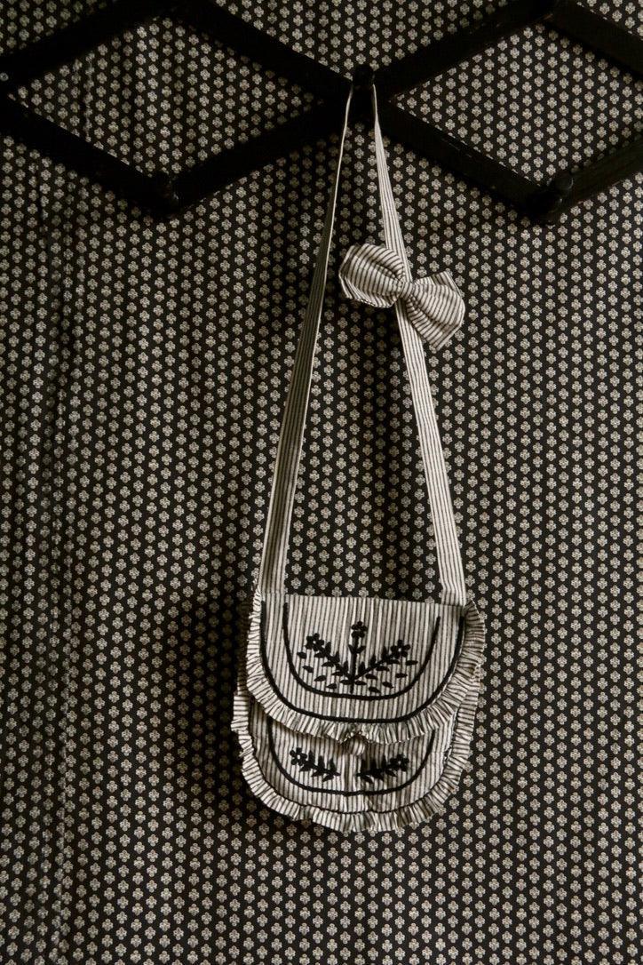 Striped fabric shoulder bag with embroidered floral design and bow, hanging on patterned wall