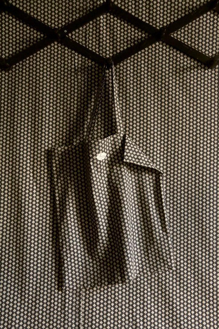 Black tote bag with small white floral print hanging on patterned background