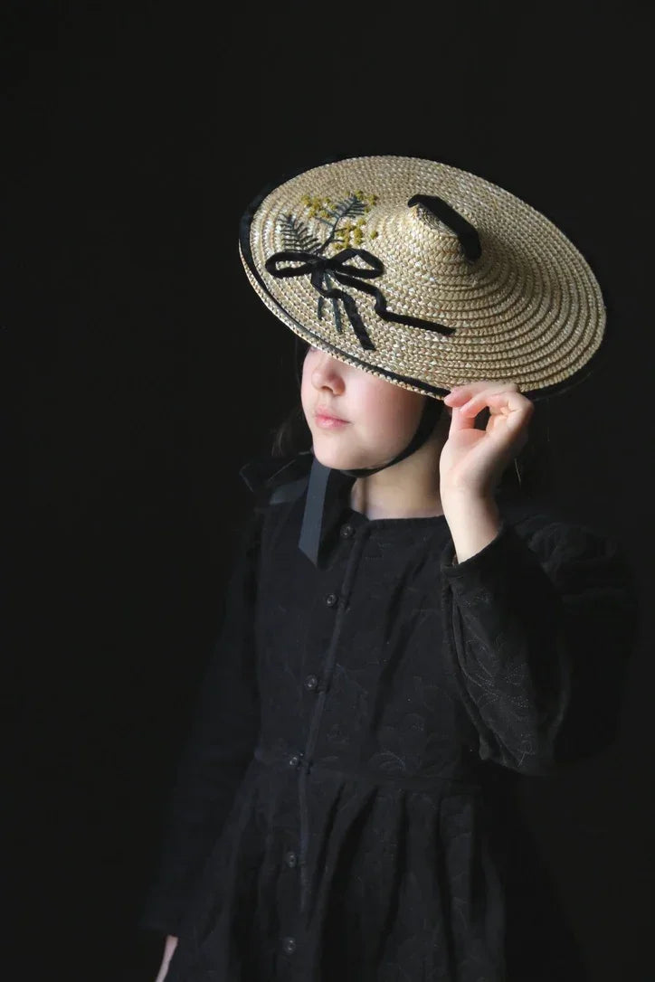 Girl in black dress wearing wide-brim straw hat with black ribbon and floral detail