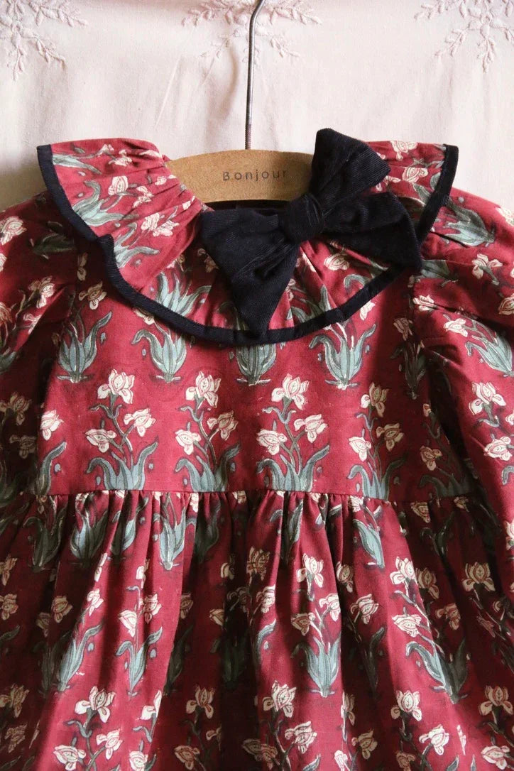 Red floral print children's dress with a ruffled collar and black bow detail