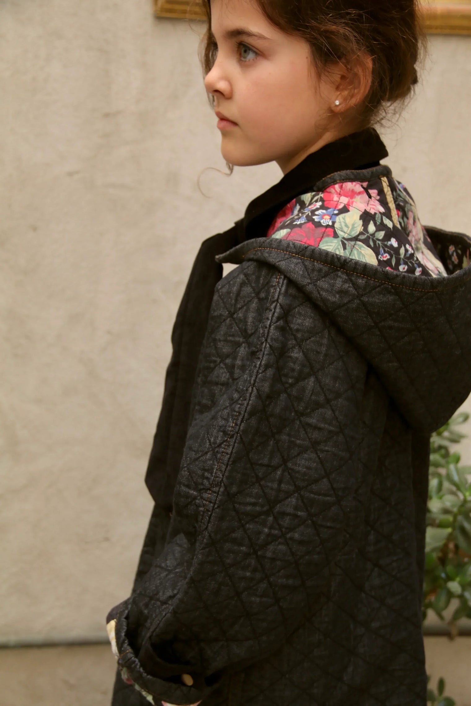Girl in quilted black hooded jacket with floral lining, standing indoors