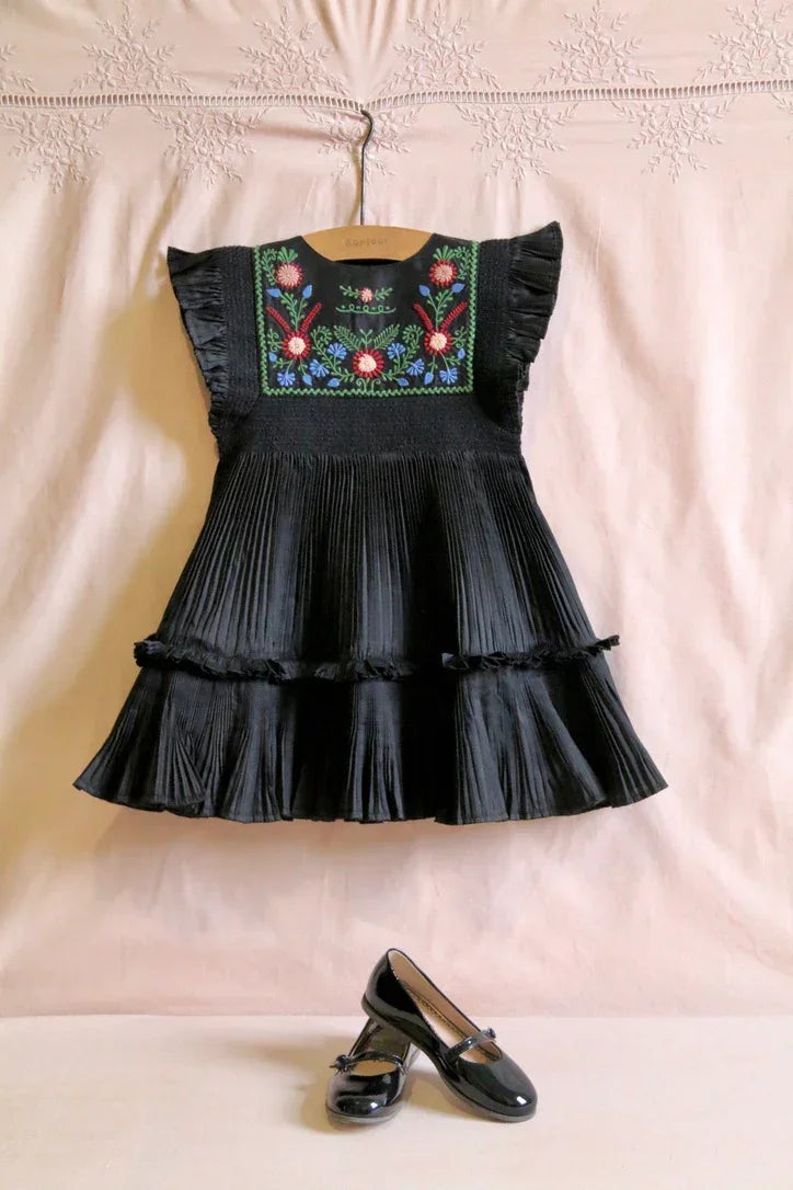Black pleated girls' dress with colorful floral embroidery, paired with black patent shoes.