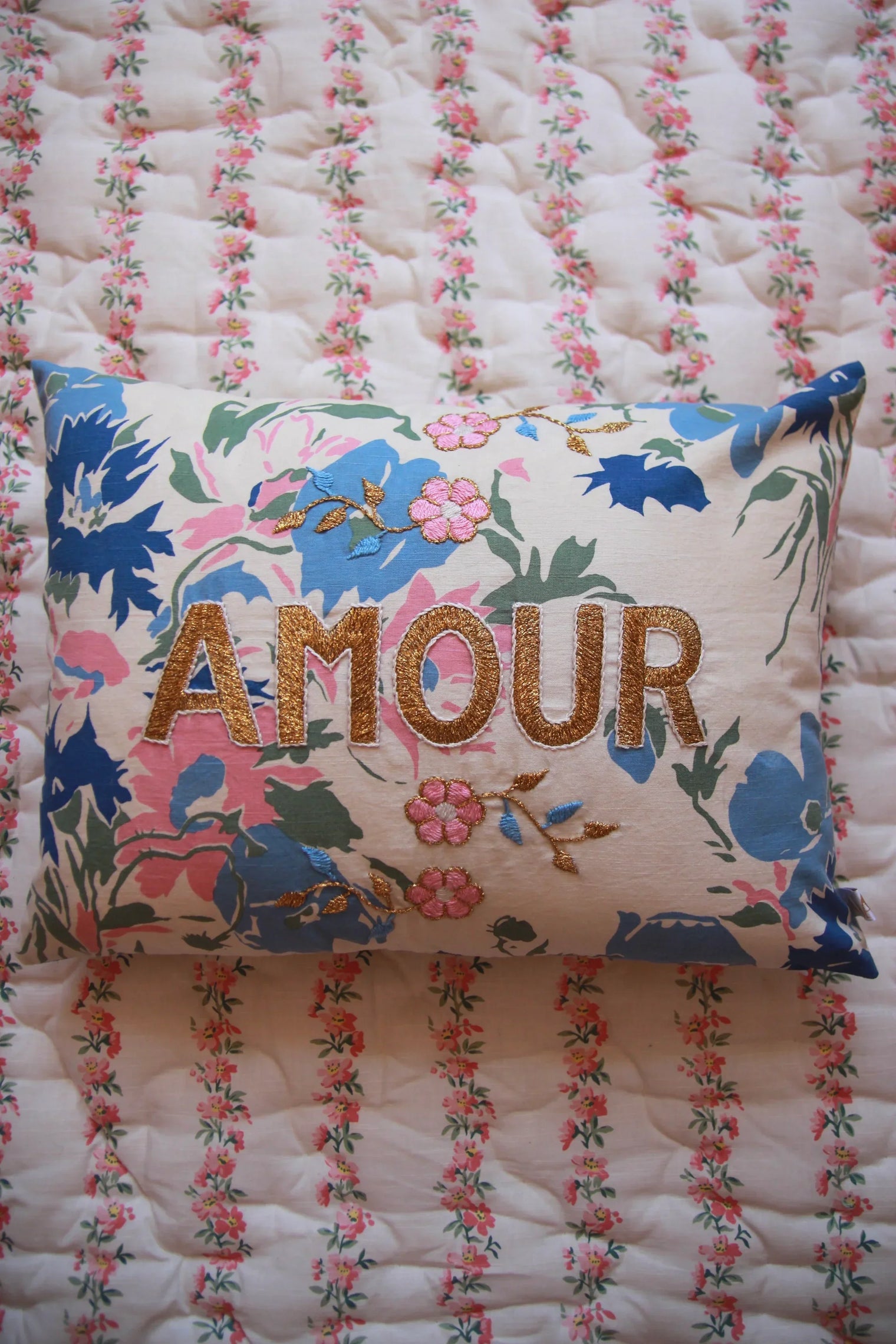 Floral embroidered cushion with gold 'AMOUR' text on quilted floral bedding