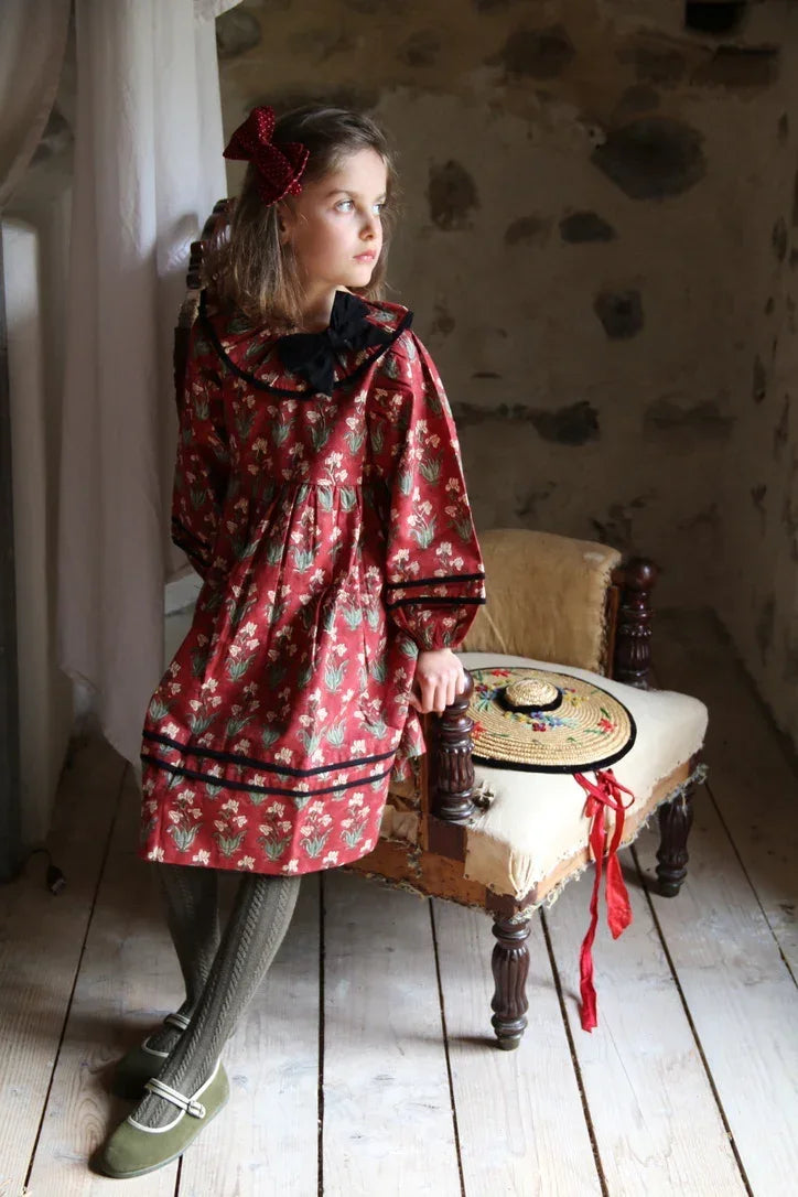 Girl in floral print red dress with black collar and bow, vintage-inspired children's fashion