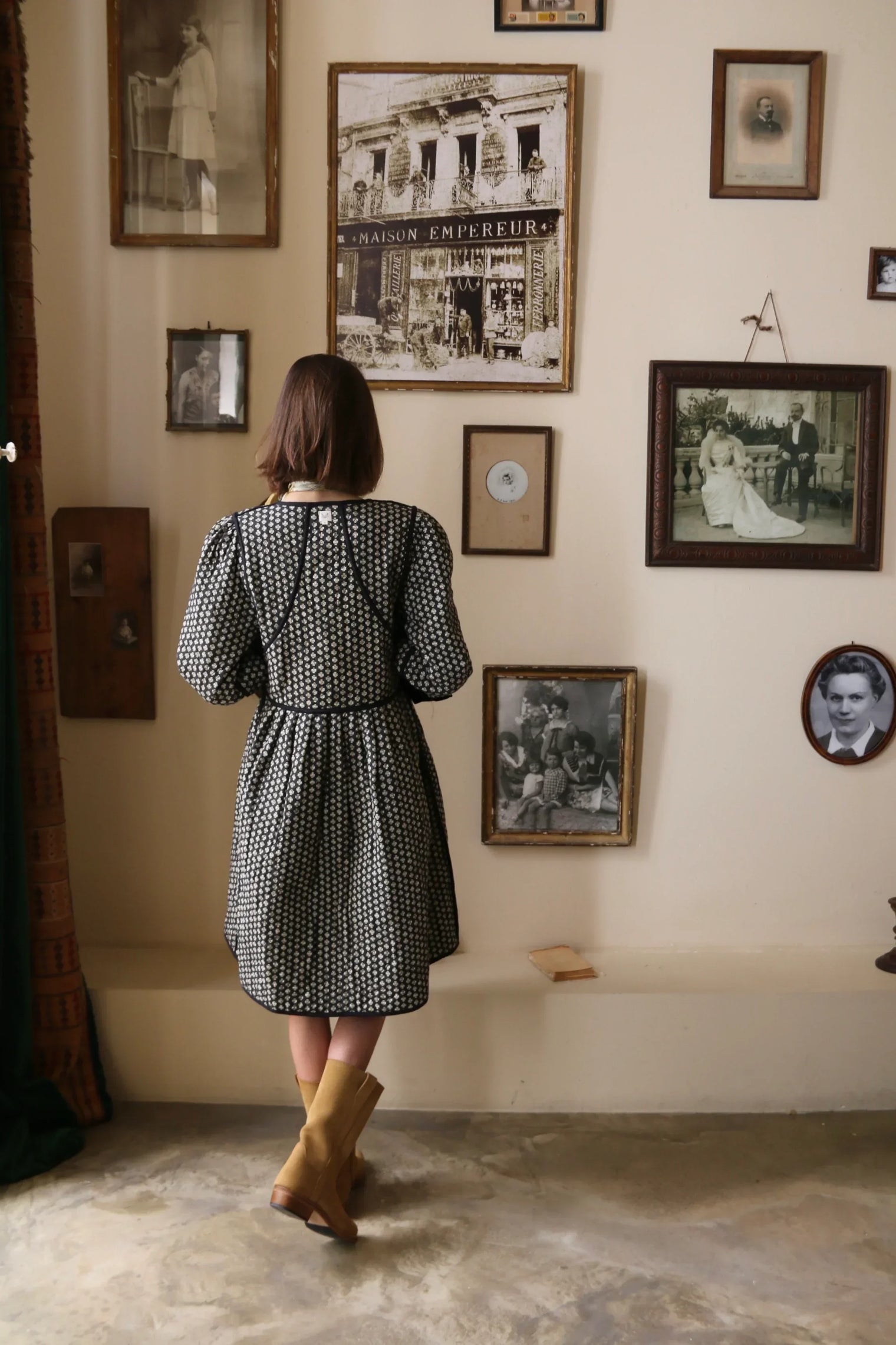 Woman in patterned dress and boots facing vintage photo wall, modern home interior