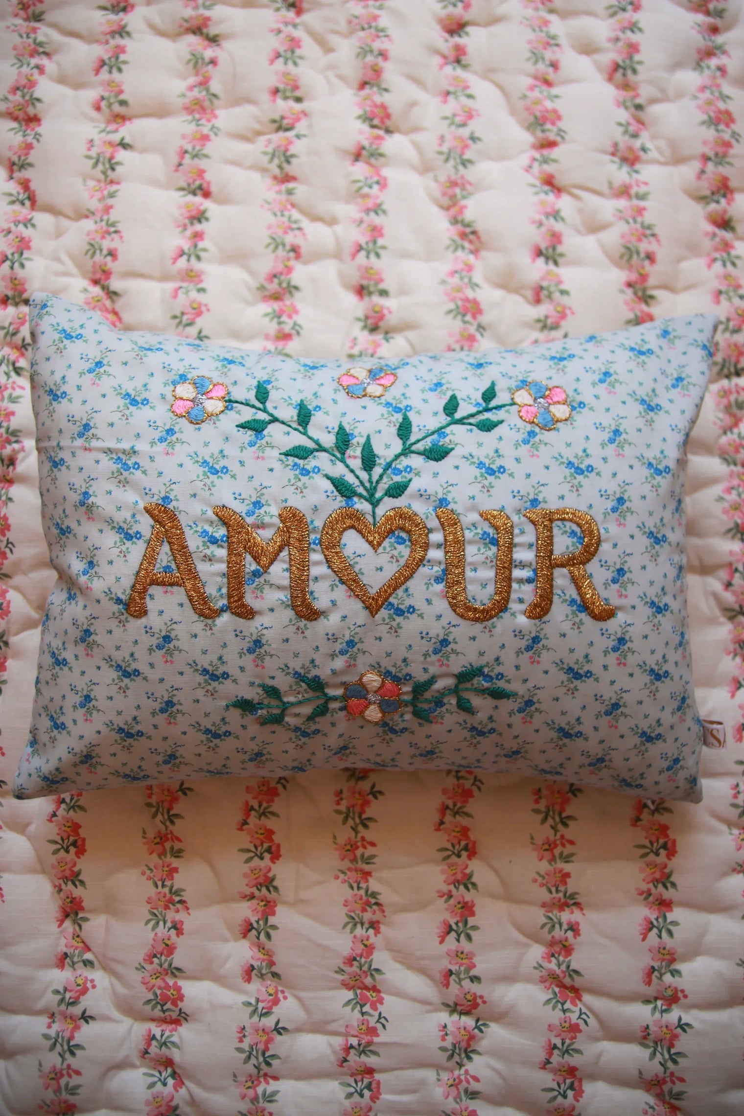 Blue floral embroidered pillow with AMOUR text on patterned pink floral quilt