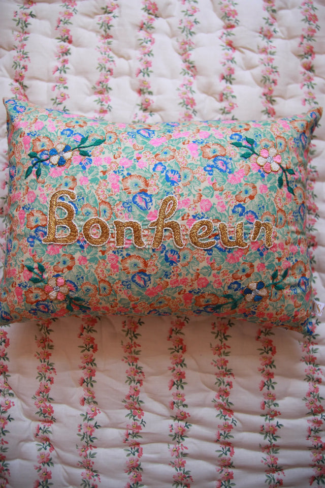 Floral embroidered pillow with 'Bonheur' text on a quilted floral bedding background