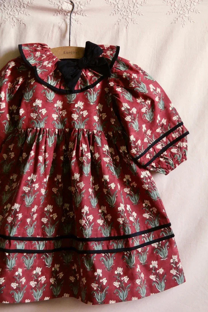Floral print maroon girls dress with black trim and bow, vintage-inspired design on hanger