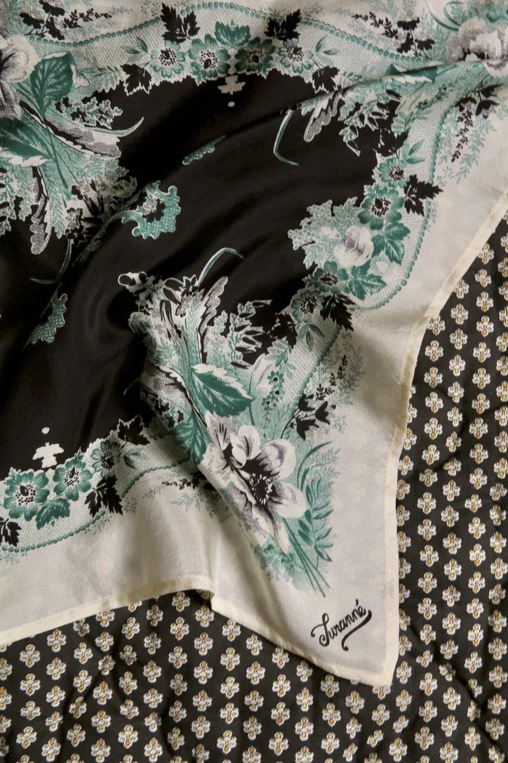 Floral print linen scarf with green and black details, laid on patterned fabric background