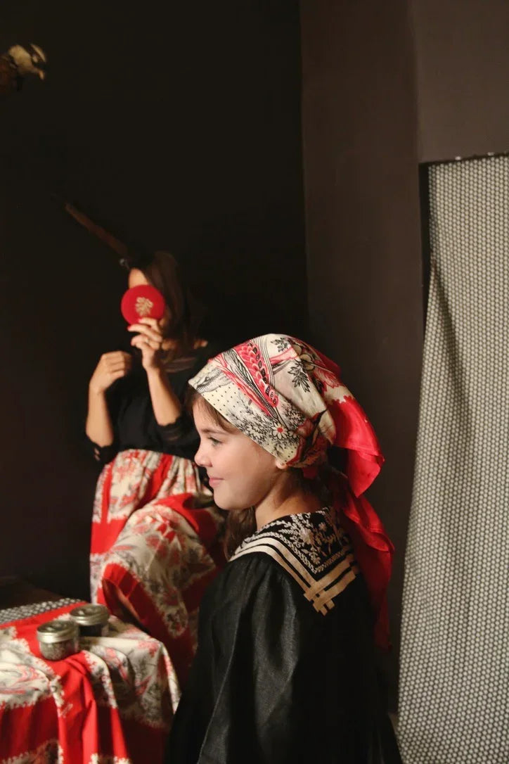 Girl in vintage-inspired children's dress and printed headscarf, with patterned table linen