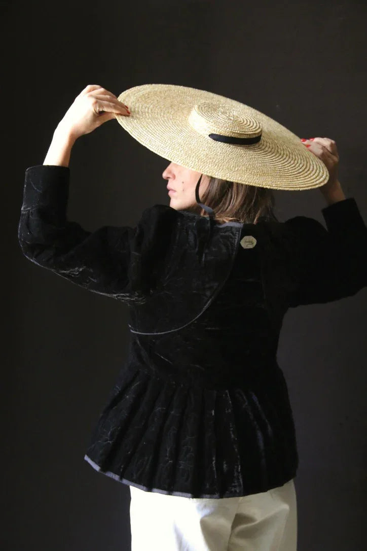 Woman in black velvet jacket and wide-brim straw hat, side view, dark background