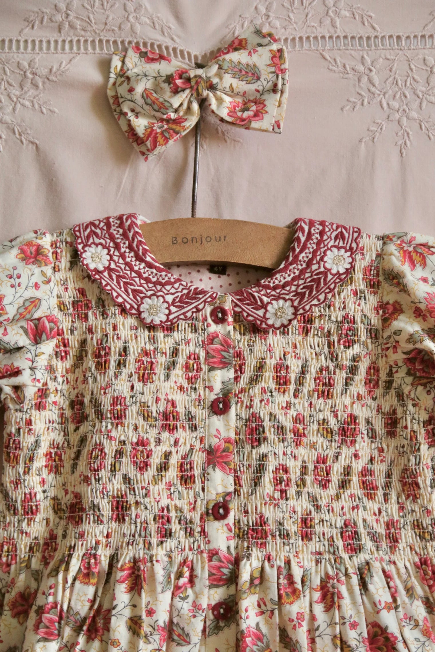 Floral smocked girls dress with embroidered collar and matching hair bow on hanger