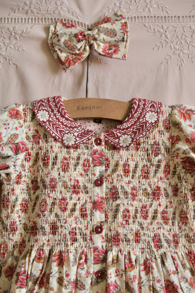 Floral smocked girls dress with embroidered collar and matching hair bow on hanger