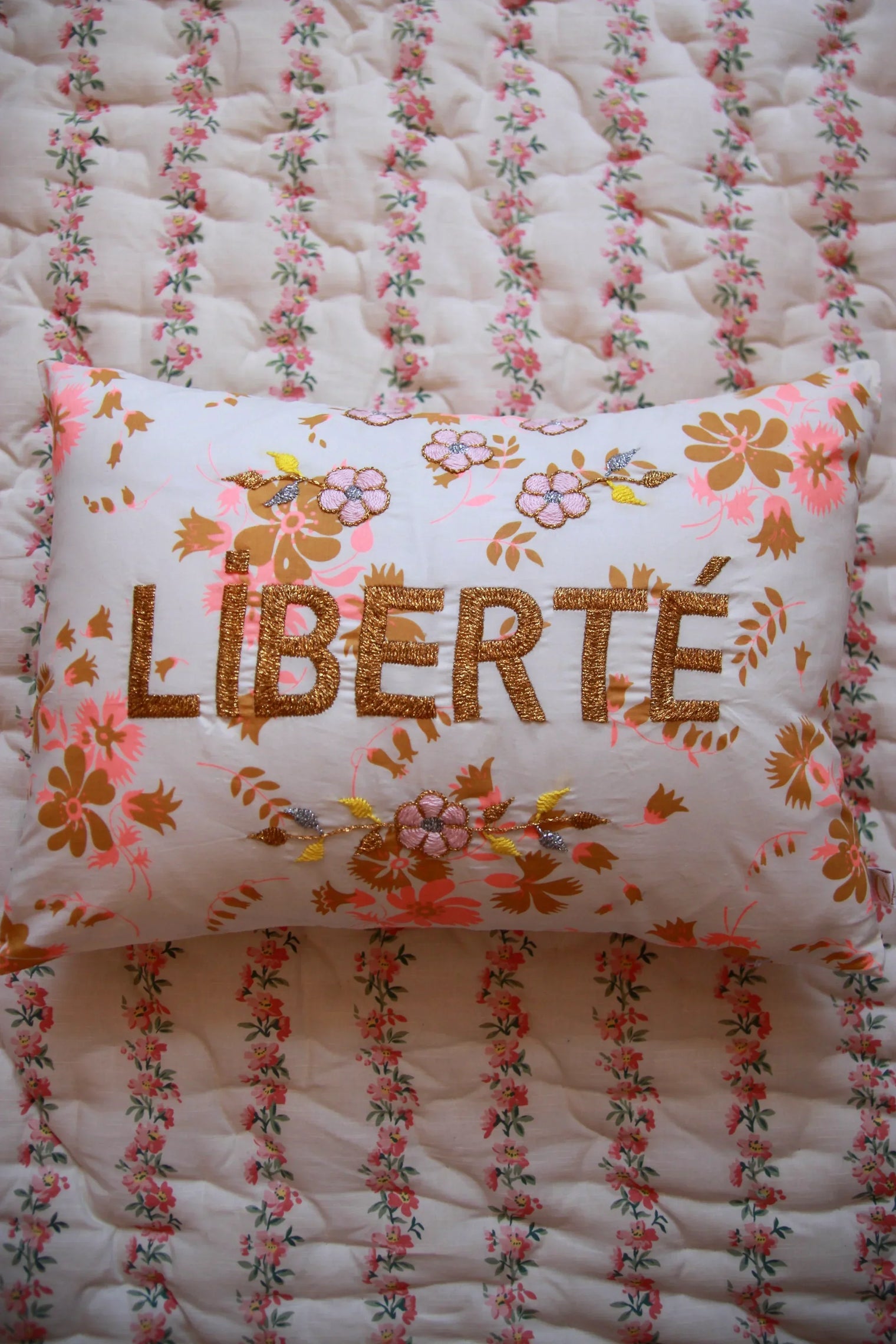 Floral embroidered LIBERTÉ pillow on pink and white patterned quilted bedding