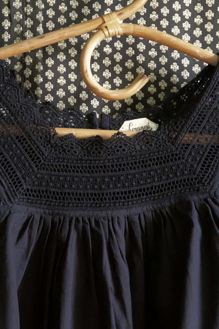 Black cotton dress with intricate lace yoke on a wooden hanger, floral patterned background