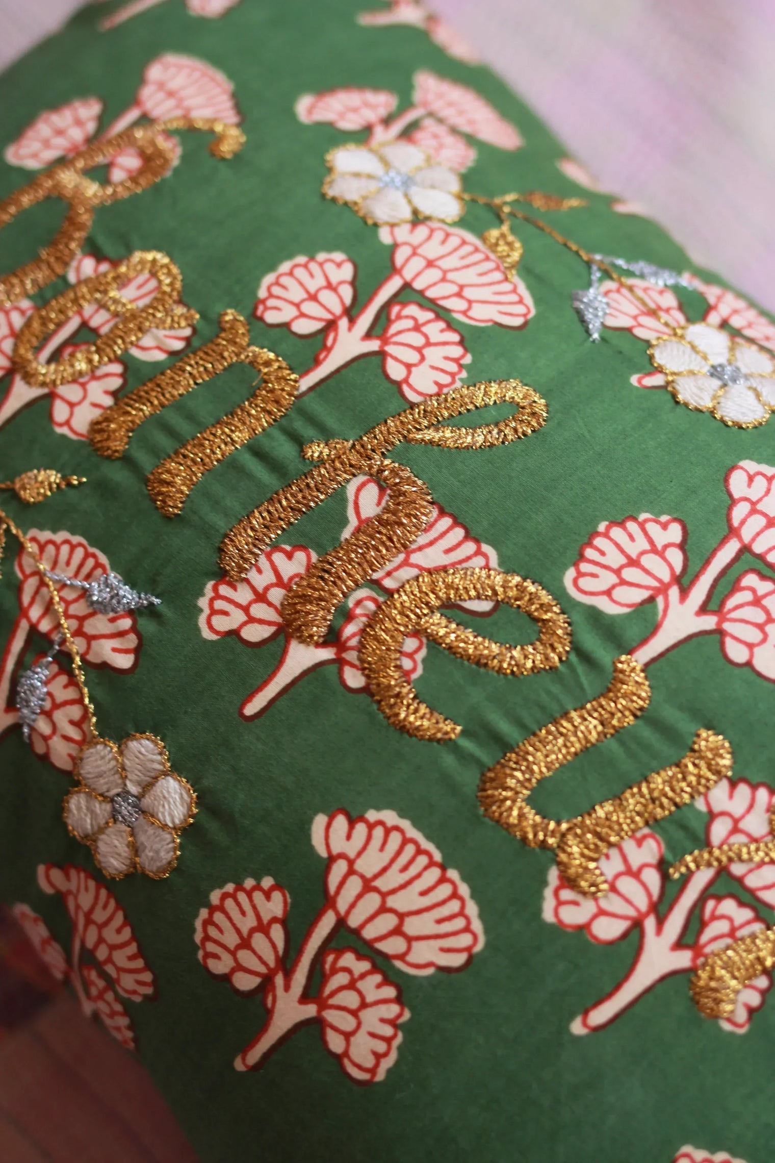 Green cushion with embroidered gold text and floral pattern, decorative home linen