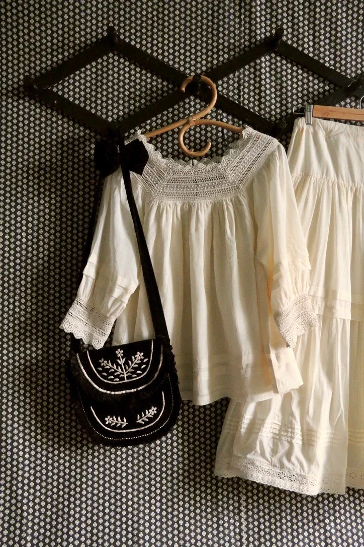 Cream embroidered blouse and skirt with black floral crossbody bag hanging on patterned wall