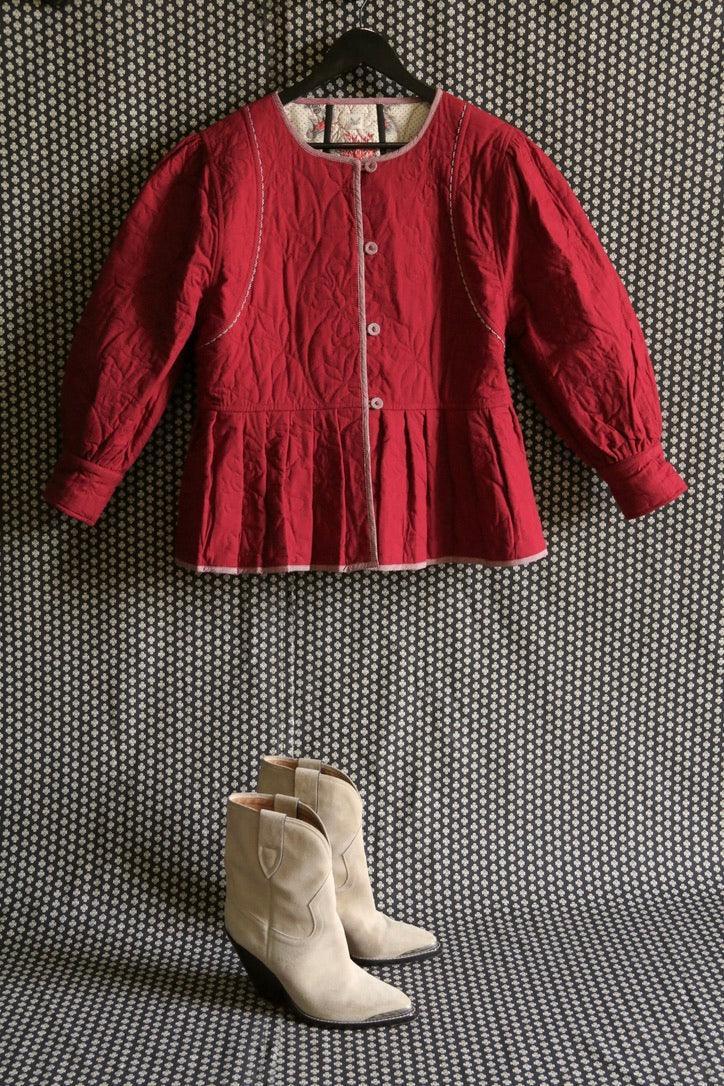 Red quilted girls jacket with buttons and cream suede boots on patterned background