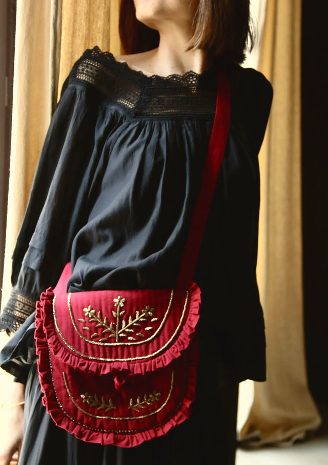 Woman wearing a black lace dress with a red embroidered ruffle crossbody bag
