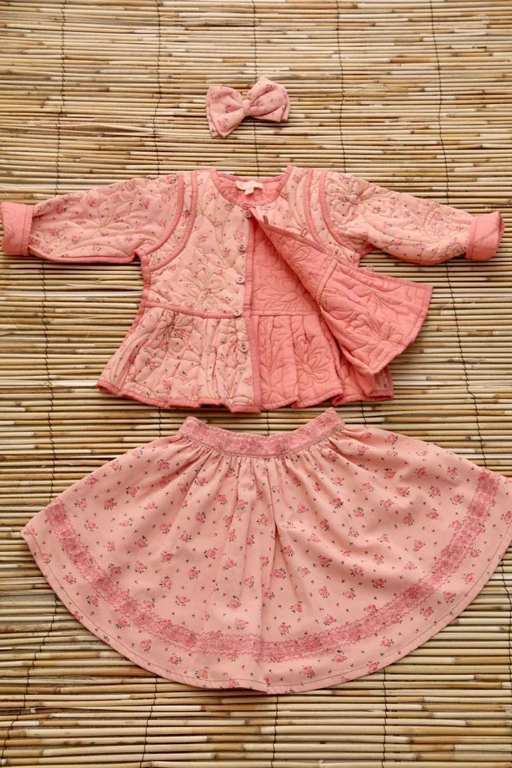 Pink floral quilted jacket, matching skirt, and hair bow set for children on bamboo mat