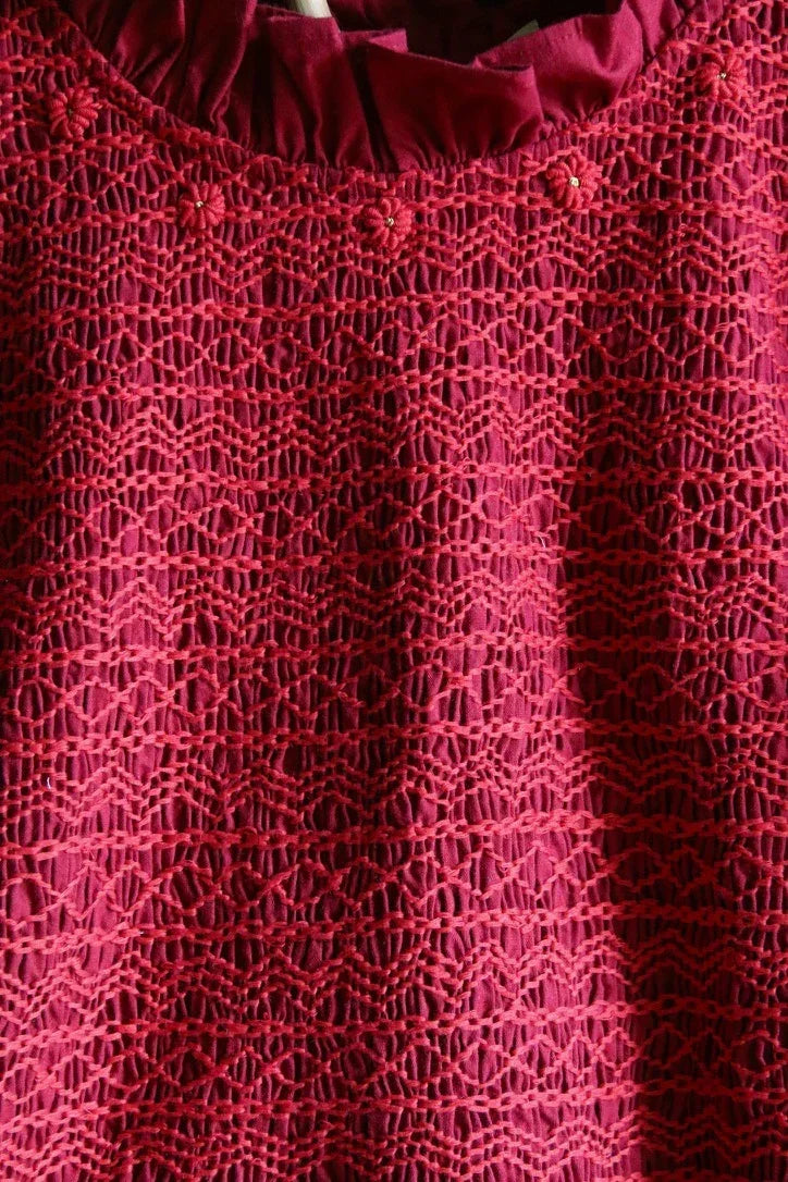 Close-up of maroon crochet lace fabric with floral embroidery and ruffled neckline