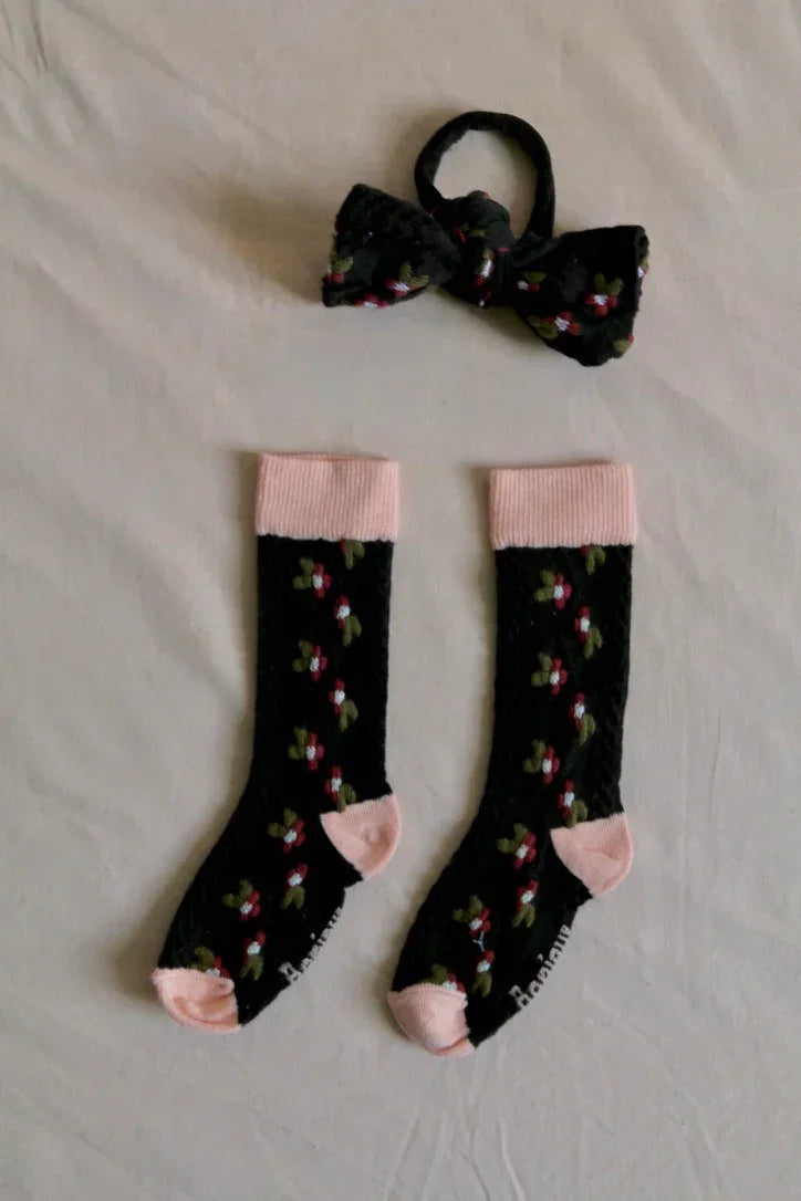 Children's black floral socks with pink accents and matching hair accessory on white background
