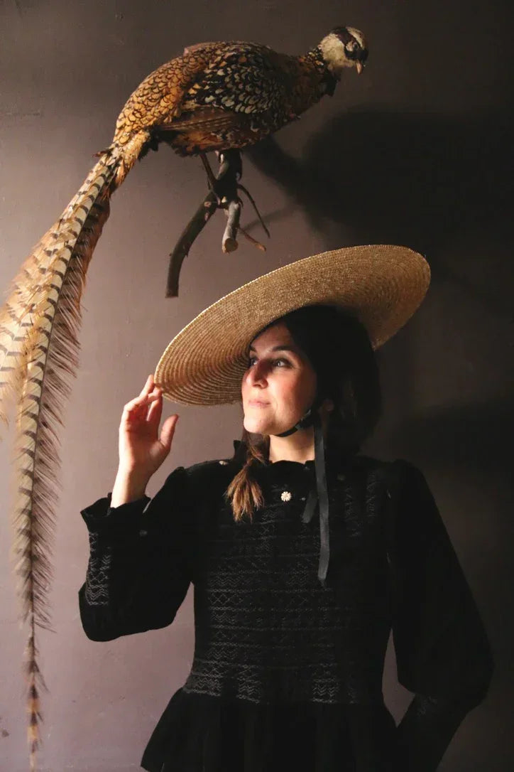 Woman in a black dress and wide-brim straw hat under mounted pheasant, vintage decor style