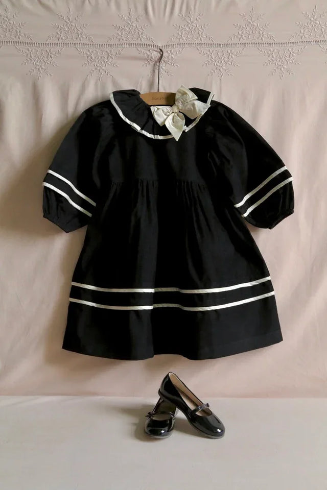 Black girls dress with white ribbon details and bow, paired with black patent shoes.