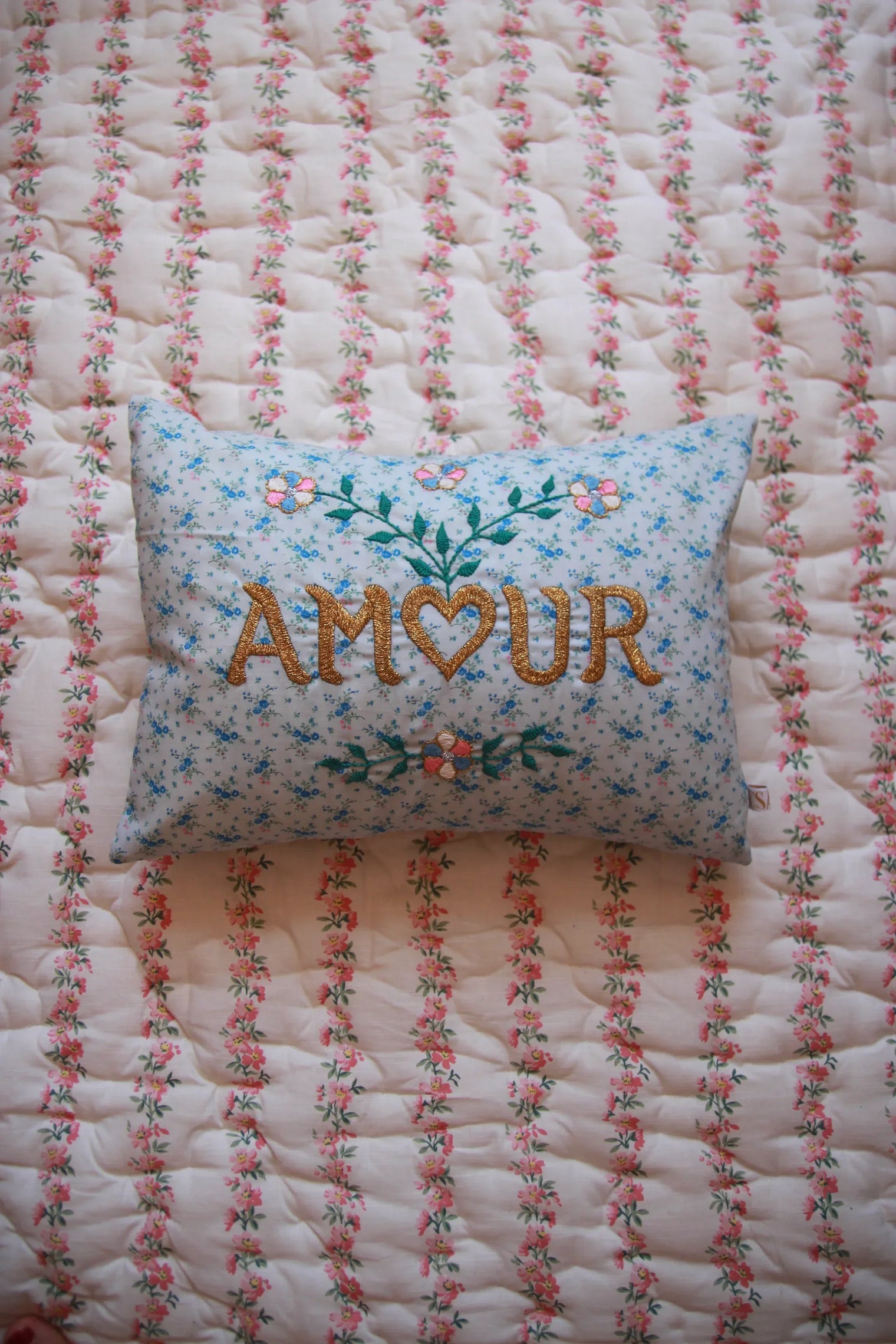 alt
Embroidered blue floral pillow with 'AMOUR' on pink floral quilted bedding