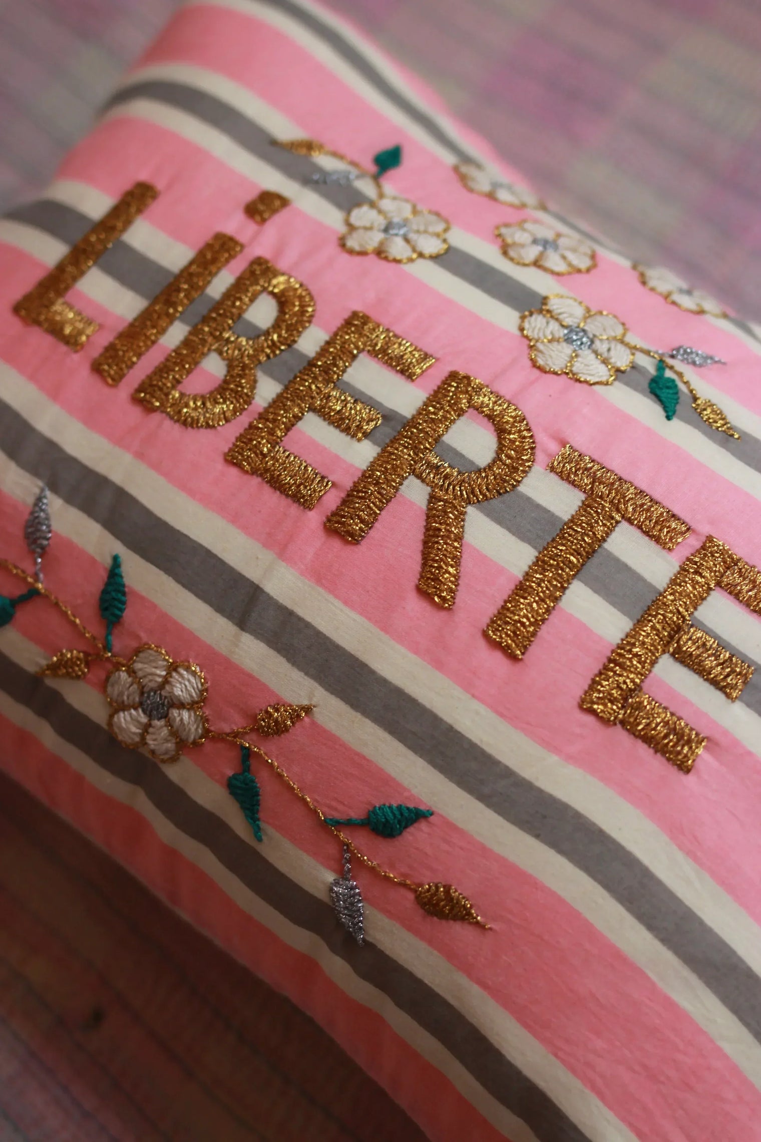 Striped pink cushion with gold-embroidered LIBERTE and floral accents, decorative home linen