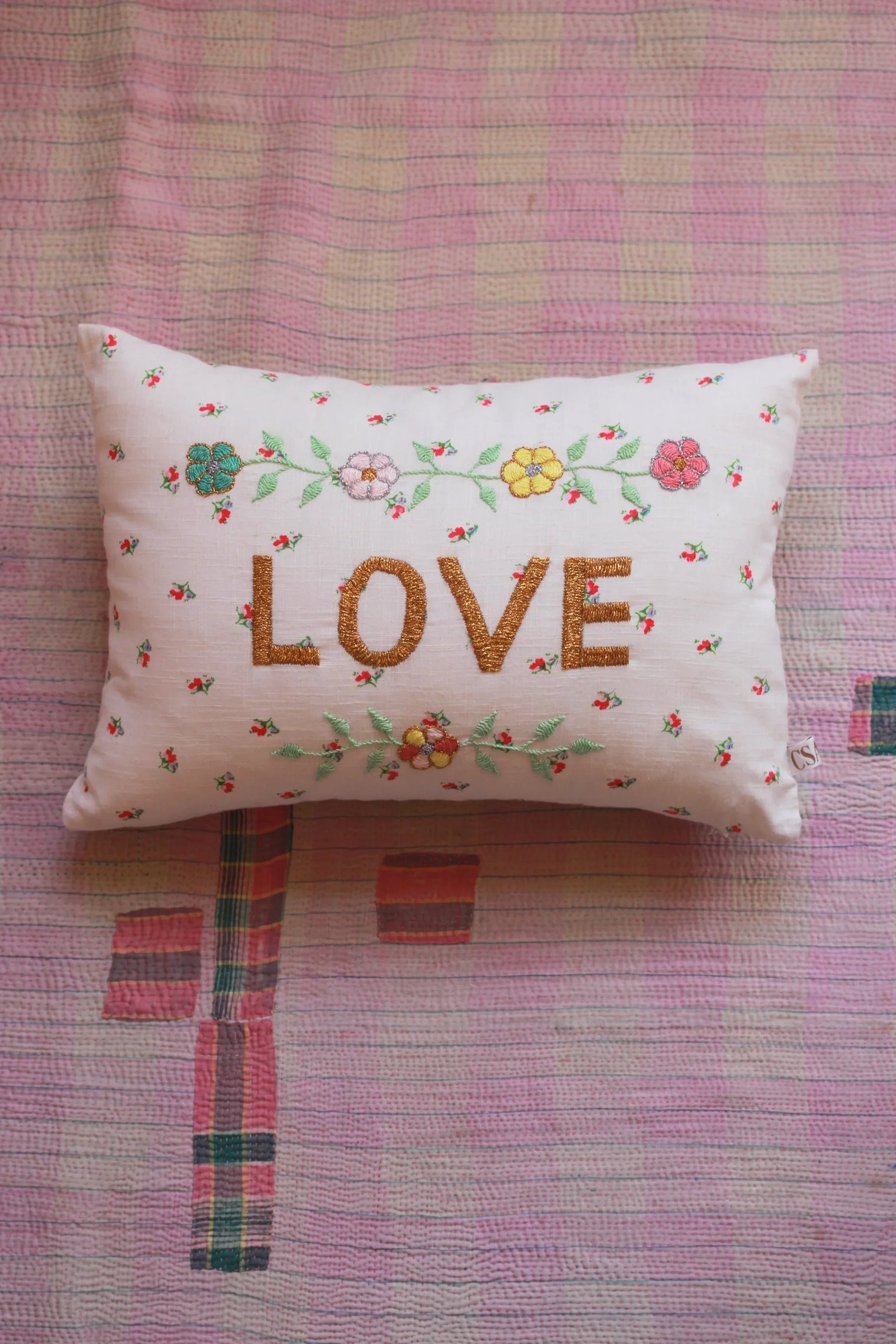 Embroidered decorative pillow with LOVE text and floral designs on pink patterned quilt
