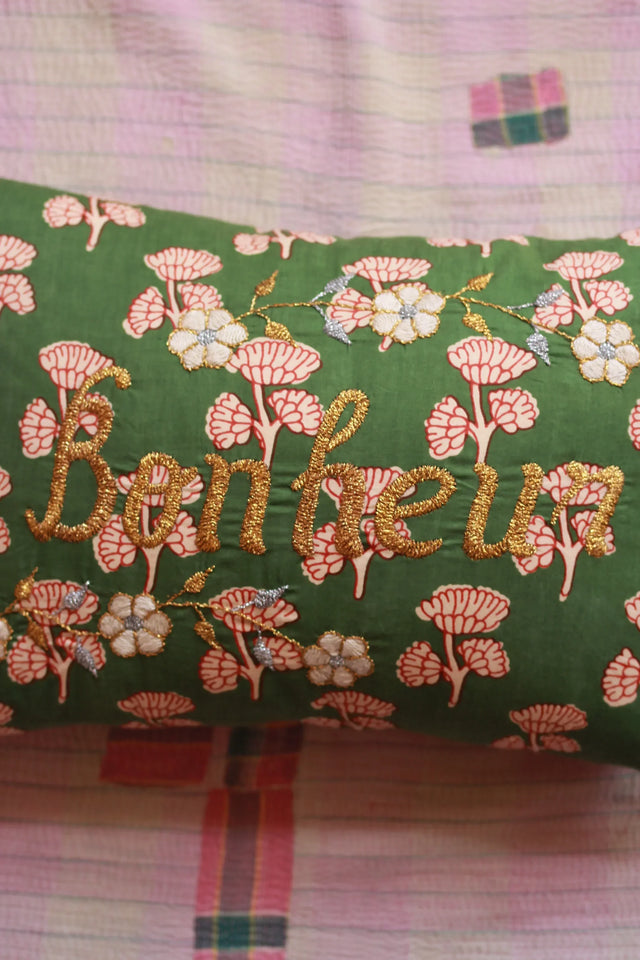 Green floral embroidered cushion with 'Bonheur' in gold script on patterned fabric