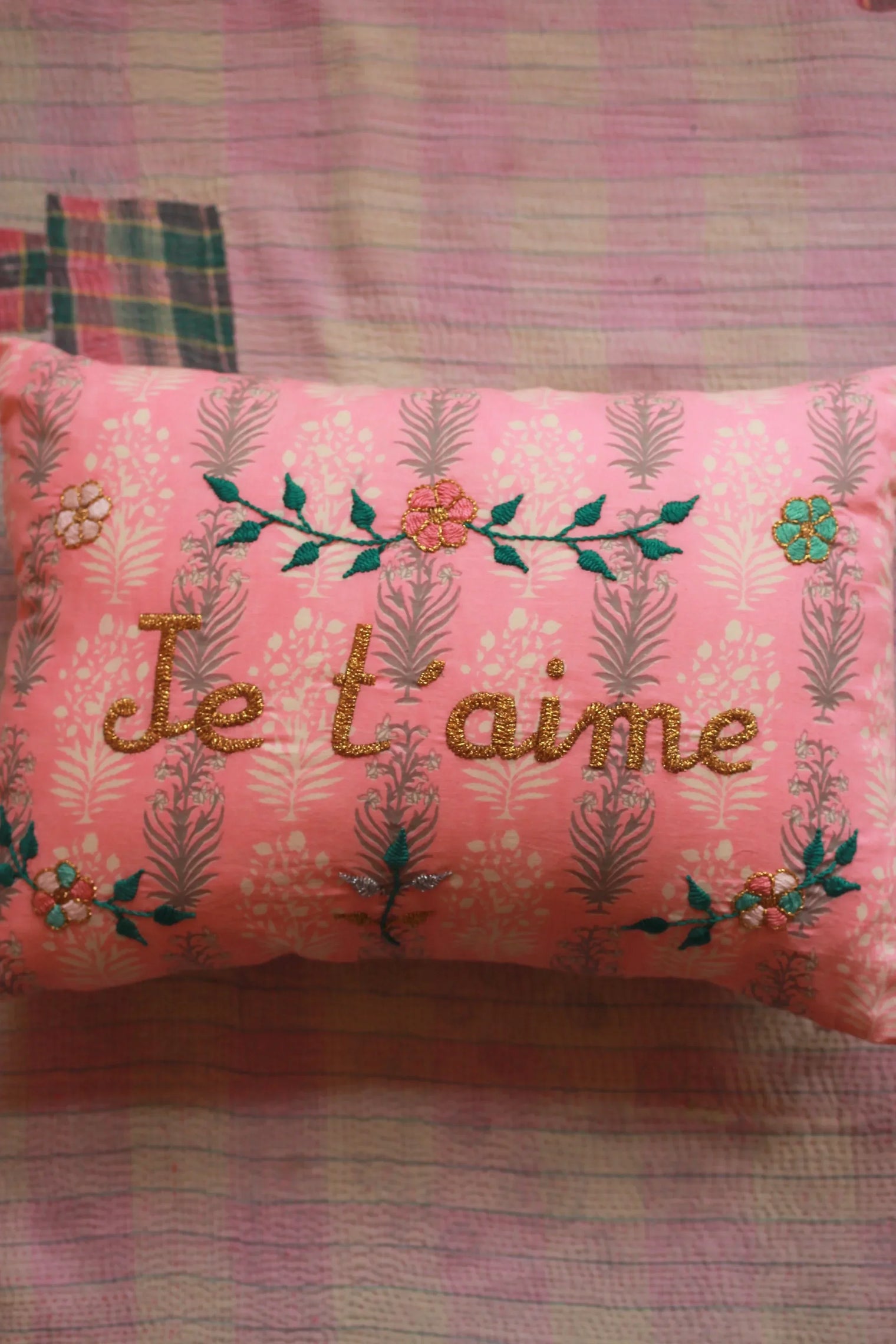 Pink embroidered floral pillow with 'Je t'aime' text on patterned linen fabric