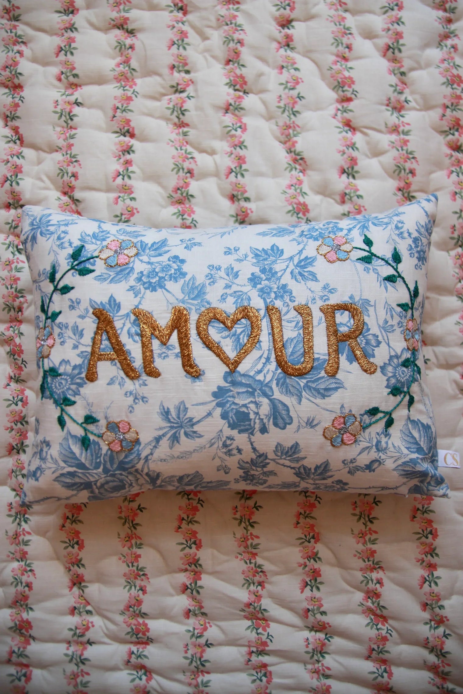 Floral blue embroidered linen pillow with 'AMOUR' text on a vintage quilted blanket