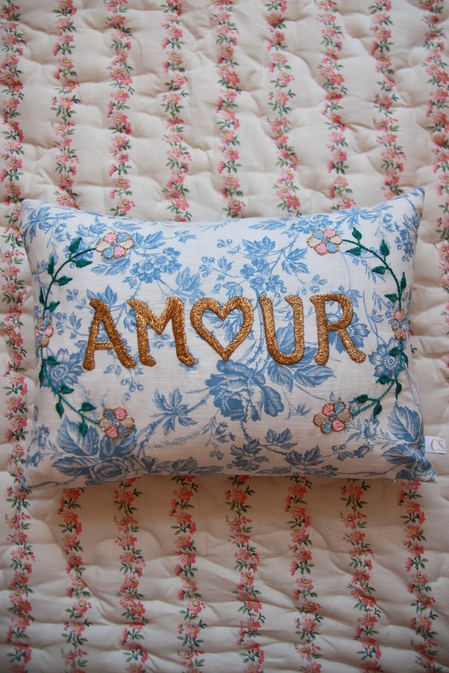Floral blue embroidered linen pillow with 'AMOUR' text on a vintage quilted blanket