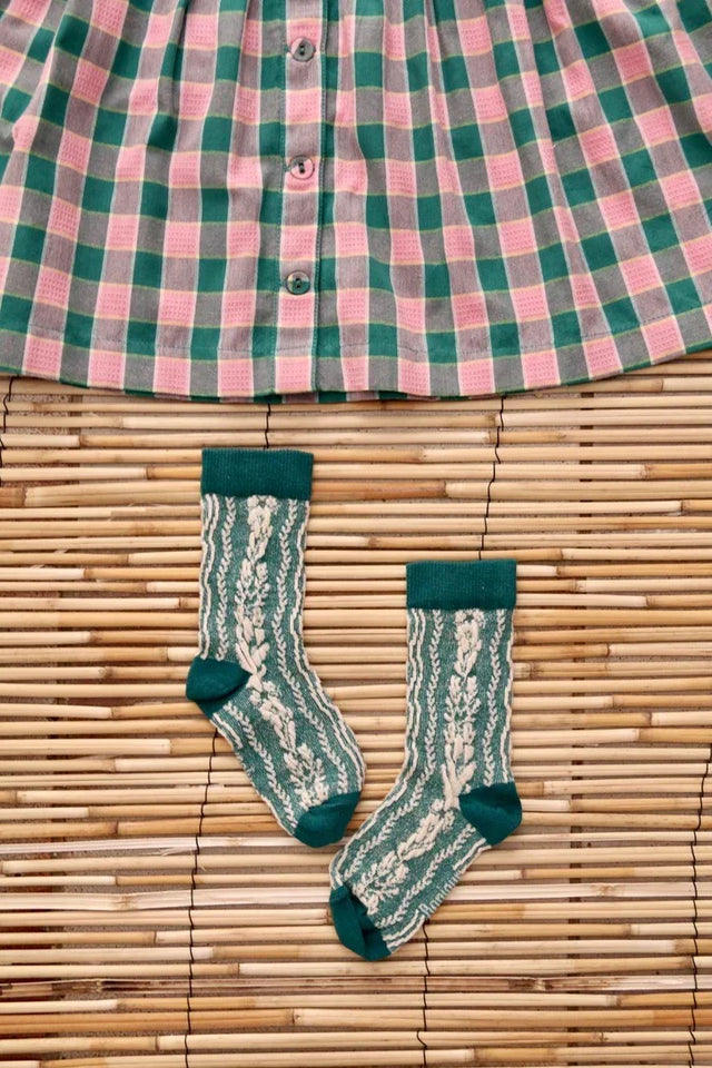 Green and cream knit socks with a leafy pattern next to a pink and green plaid skirt