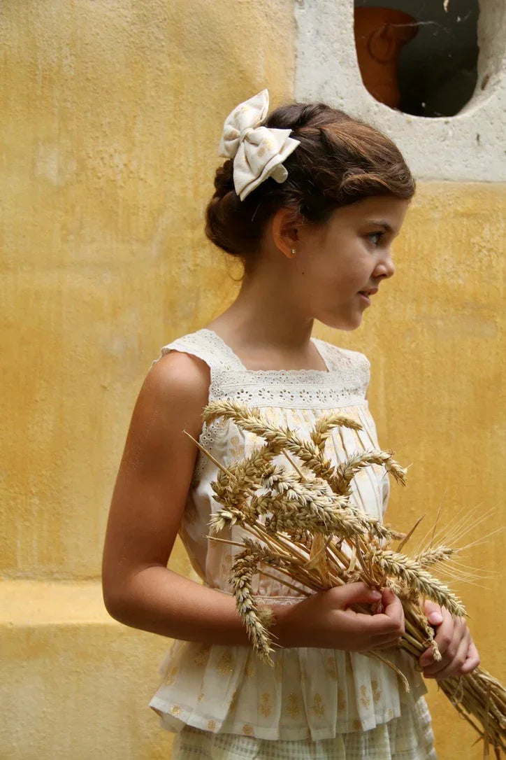 Girl in vintage-inspired sleeveless dress with bow hair accessory holding dried wheat stalks