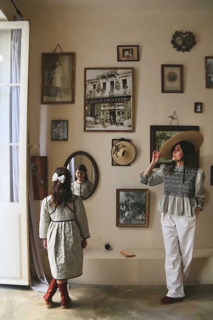 Woman in wide-brim hat and girl in printed dress in vintage-inspired room with gallery wall