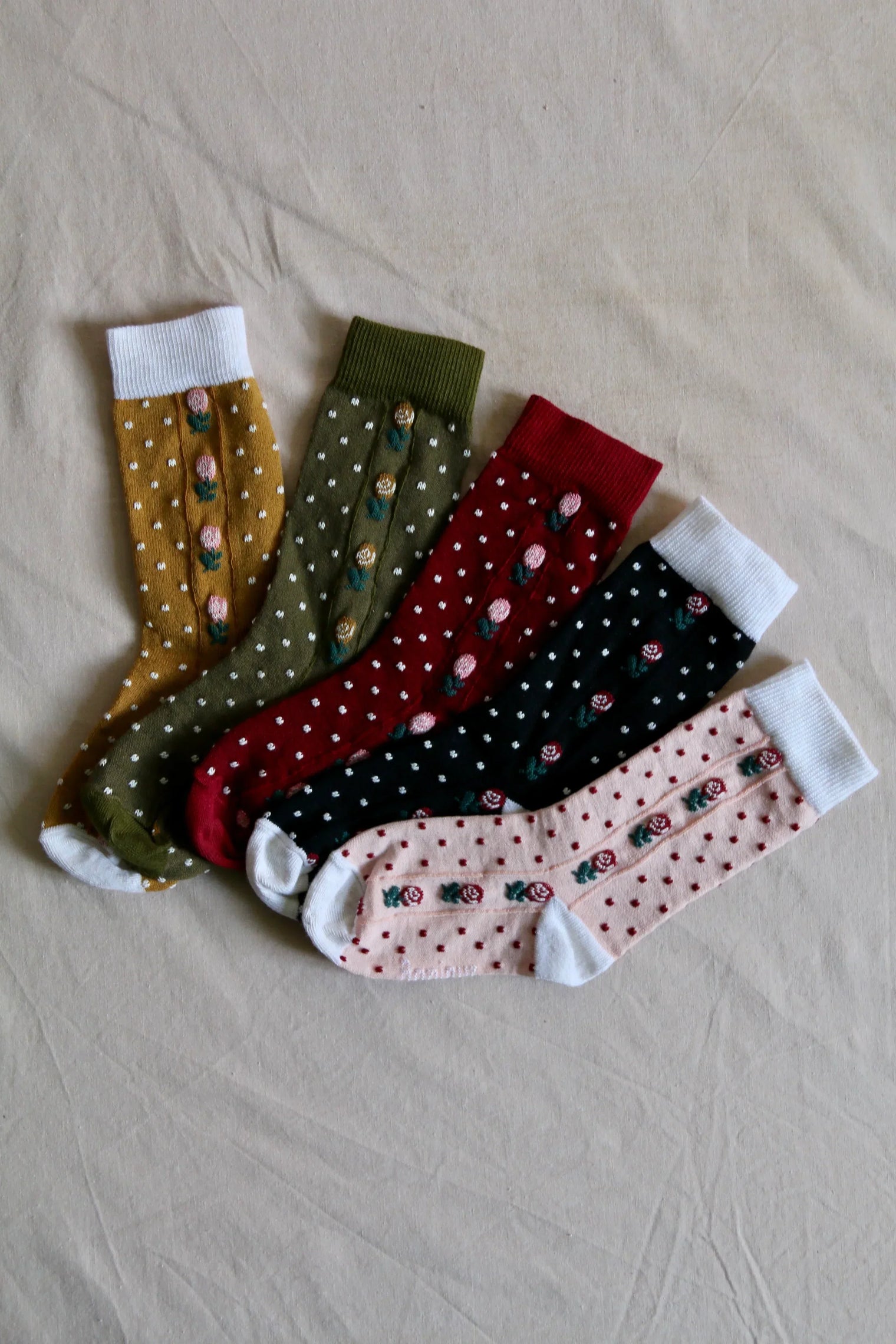 Assorted floral patterned children's socks in various colors on a beige fabric background