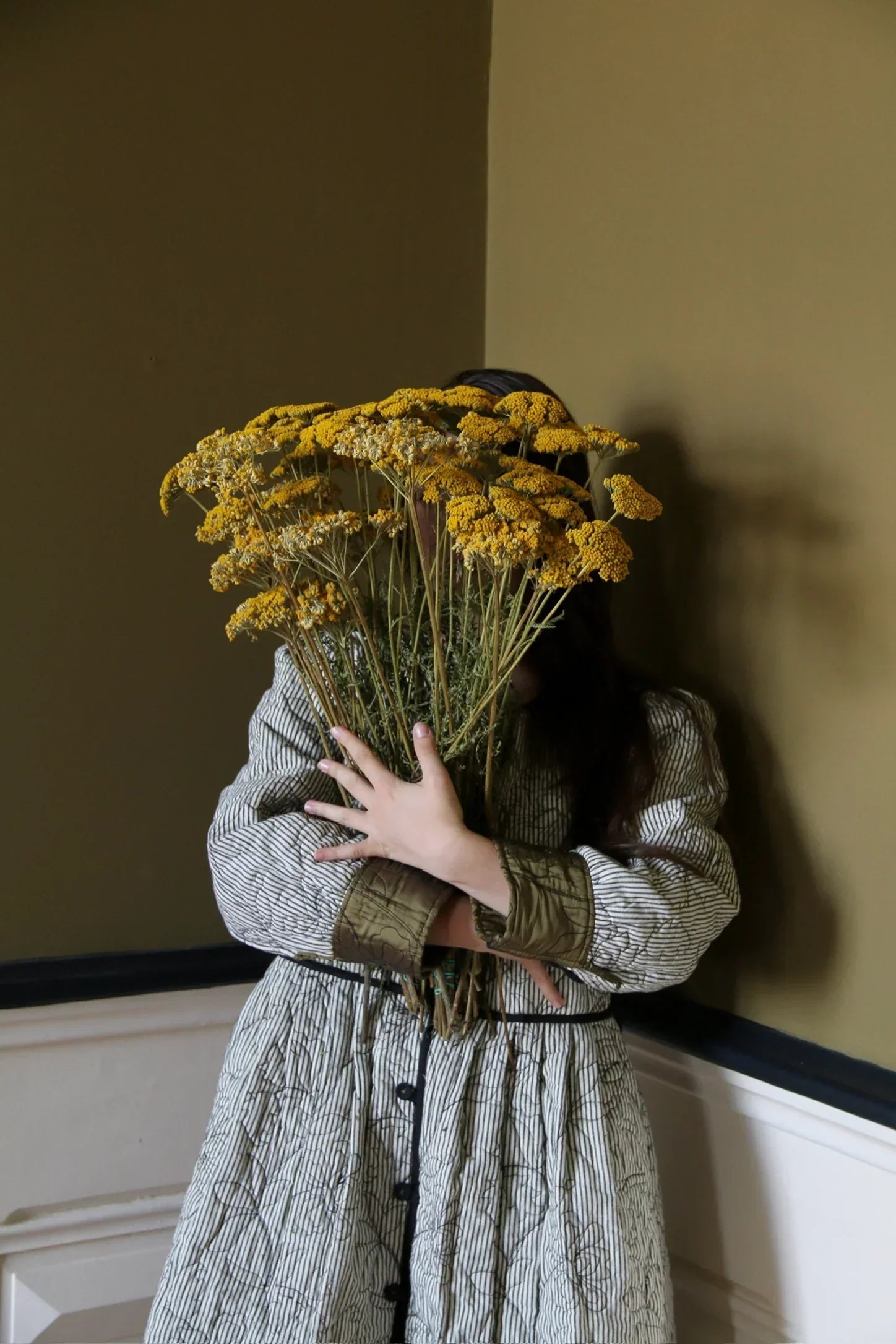 Child in striped dress holding bouquet of yellow flowers in a neutral-toned room