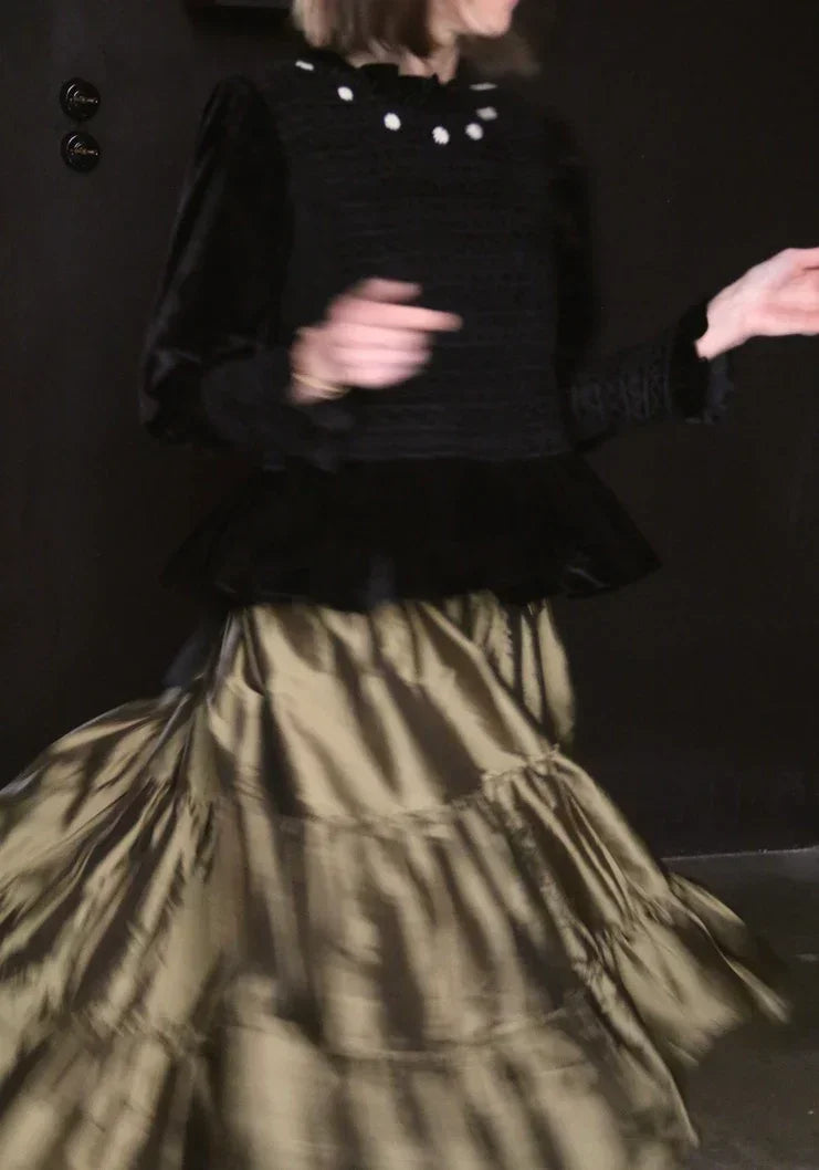 Woman in black velvet top with white collar accents and flowing olive tiered skirt, mid-movement