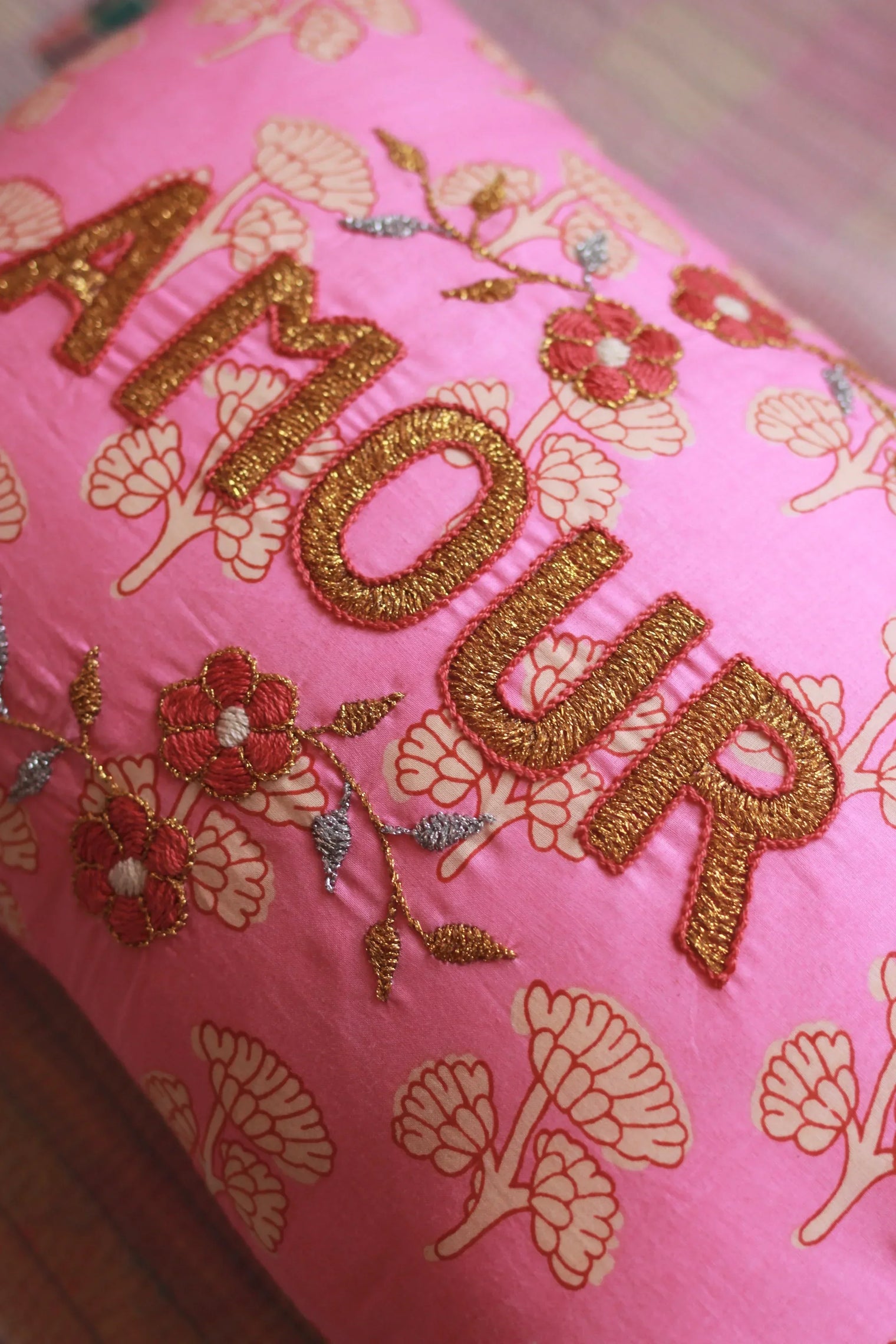 Pink decorative pillow with gold embroidered "AMOUR", floral patterns, and stitched flowers