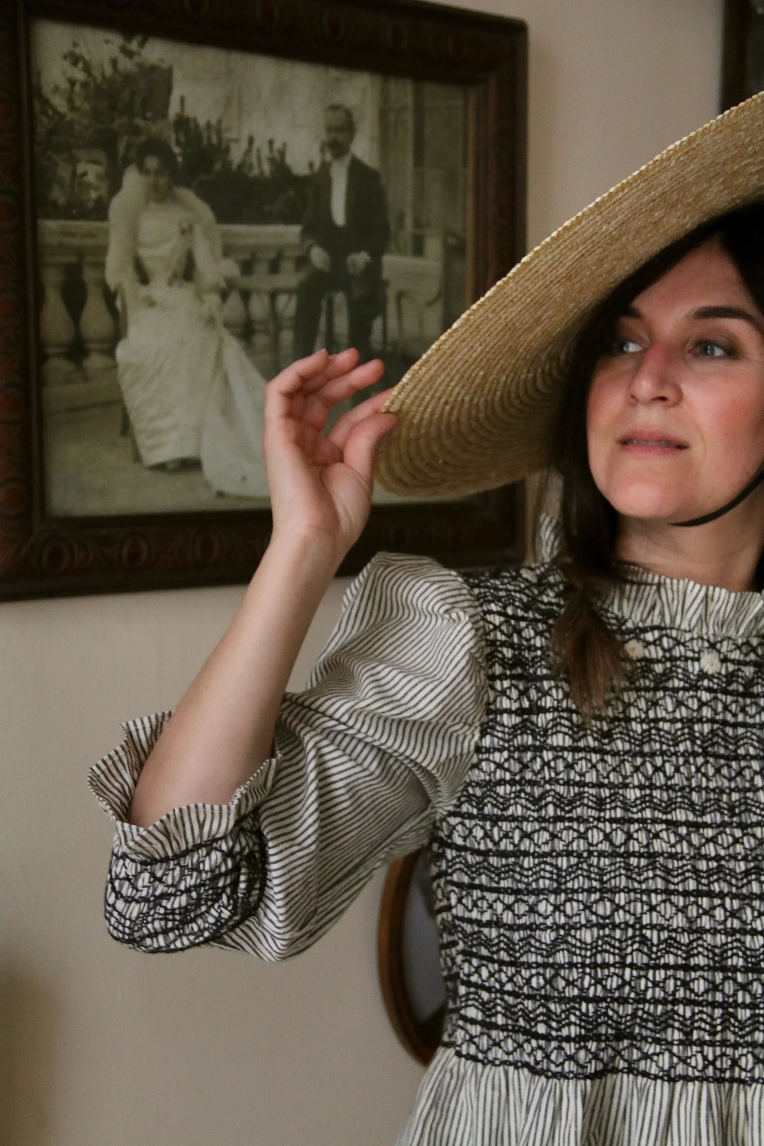 Woman in striped dress with smocking and wide-brim straw hat, vintage portrait in background