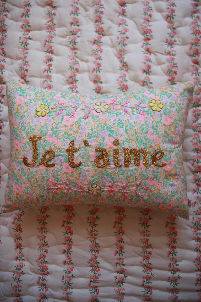 Floral decorative pillow with 'Je t'aime' embroidered in gold on a patterned quilted bedspread