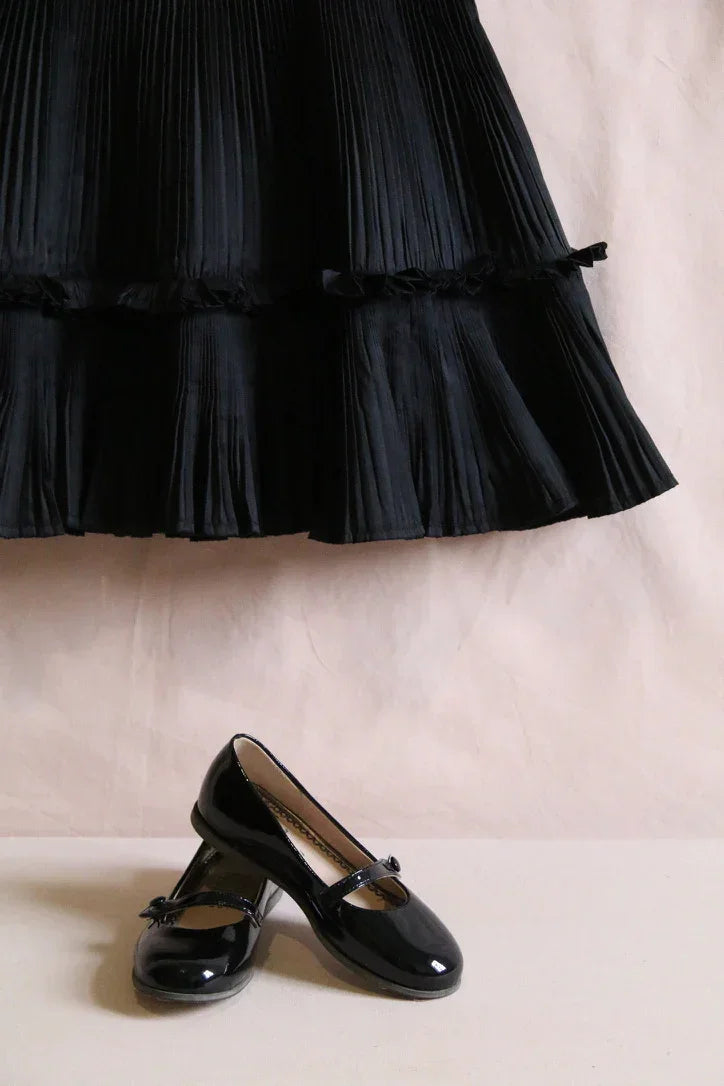 Girls black pleated skirt and glossy black Mary Jane shoes, elegant childrenswear display.